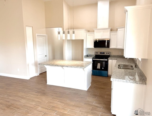 kitchen featuring a sink, stainless steel microwave, range with electric stovetop, light wood finished floors, and a towering ceiling