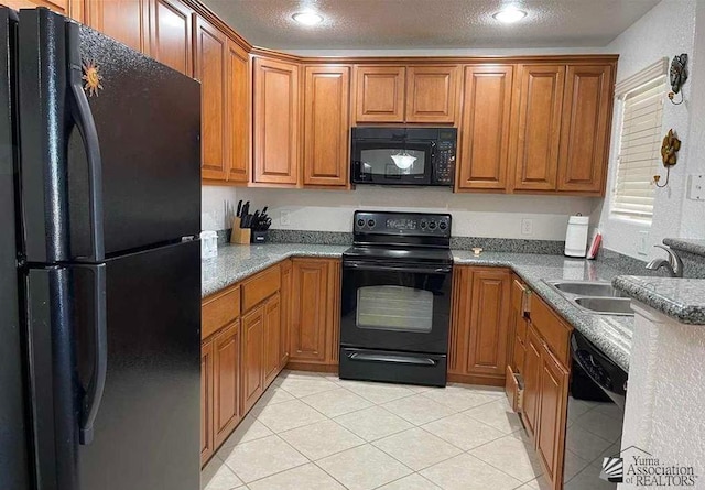 kitchen featuring brown cabinetry, a textured ceiling, black appliances, and a sink