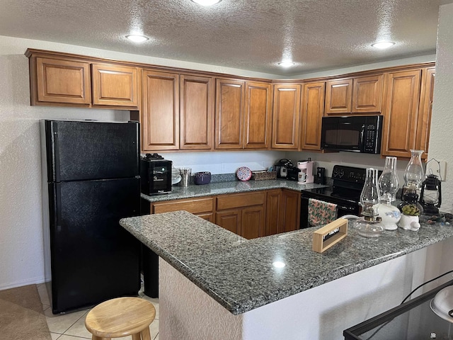 kitchen with a kitchen bar, brown cabinets, black appliances, and a peninsula