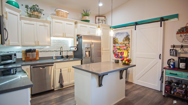 kitchen featuring white cabinets, sink, hanging light fixtures, a barn door, and appliances with stainless steel finishes