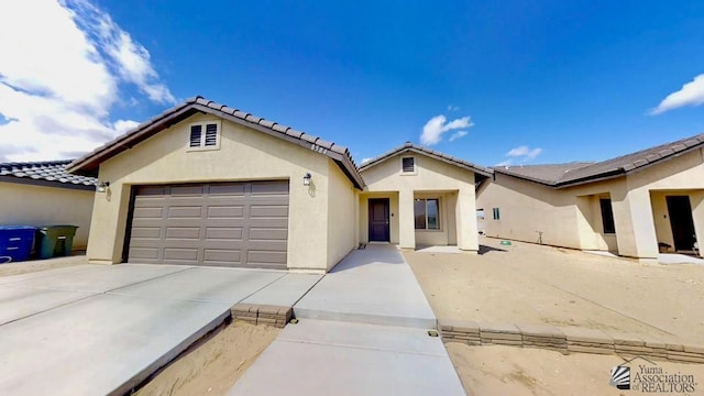 view of front of house with stucco siding, a tiled roof, driveway, and a garage