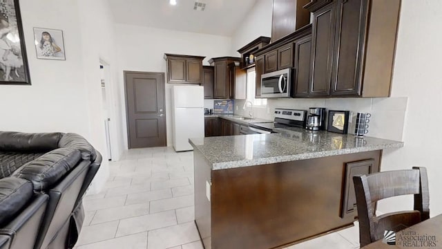 kitchen with dark brown cabinetry, open floor plan, light stone counters, a peninsula, and stainless steel appliances