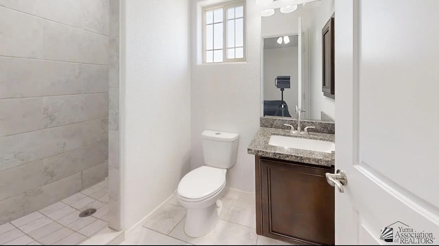 full bathroom featuring a tile shower, toilet, vanity, and baseboards