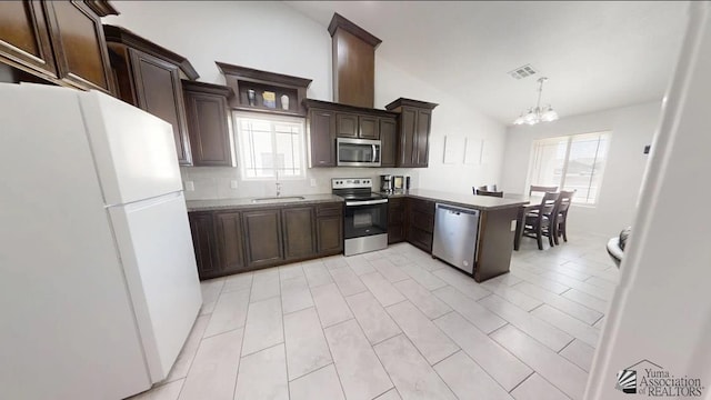 kitchen with lofted ceiling, a sink, stainless steel appliances, dark brown cabinets, and a notable chandelier