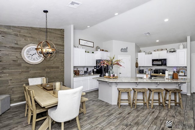 kitchen with a kitchen island with sink, light stone countertops, black appliances, white cabinets, and decorative light fixtures