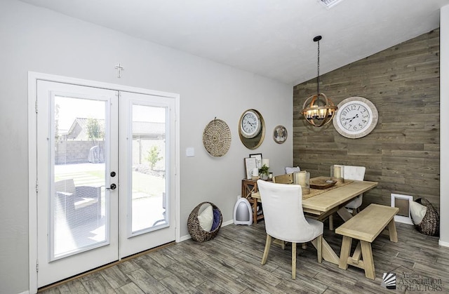 dining room featuring french doors, wood-type flooring, a chandelier, vaulted ceiling, and wooden walls