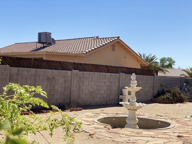 view of property exterior featuring a tile roof, fence, central AC, and stucco siding