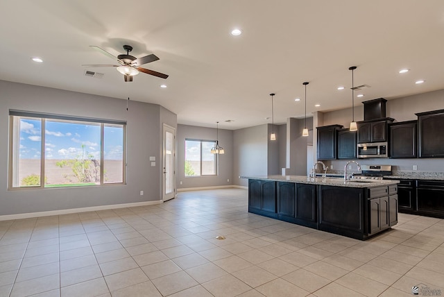 kitchen featuring light tile patterned floors, an island with sink, appliances with stainless steel finishes, ceiling fan with notable chandelier, and open floor plan