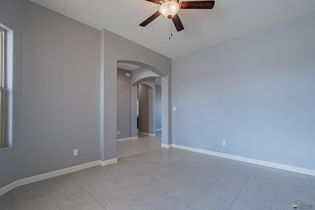 unfurnished room featuring arched walkways, light tile patterned floors, baseboards, and ceiling fan