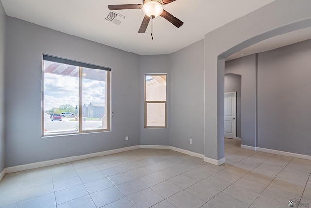 empty room featuring light tile patterned floors, baseboards, visible vents, arched walkways, and ceiling fan