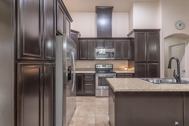 kitchen with appliances with stainless steel finishes, dark brown cabinetry, light tile patterned floors, and sink