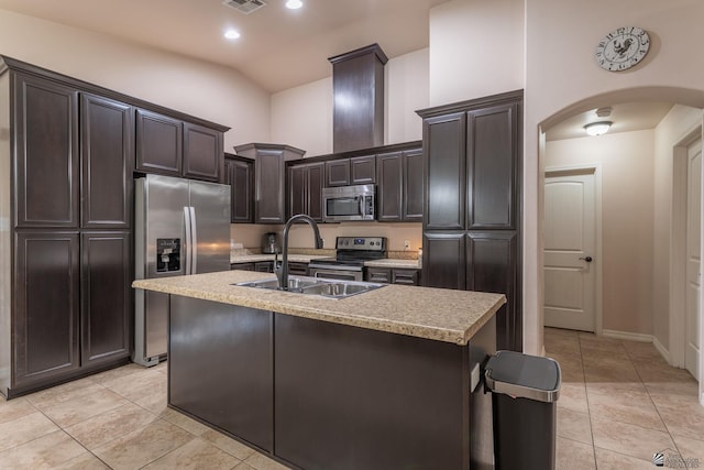 kitchen featuring sink, light tile patterned floors, an island with sink, appliances with stainless steel finishes, and dark brown cabinetry