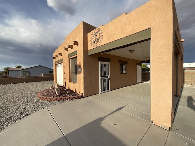rear view of house featuring stucco siding, a garage, and a patio