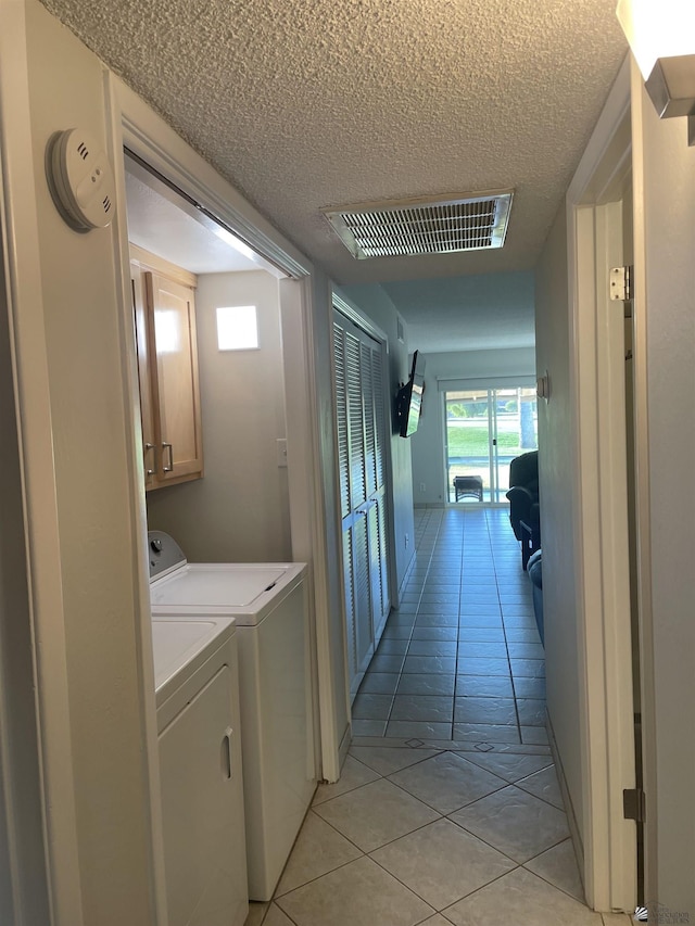 laundry room featuring washing machine and dryer, light tile patterned flooring, and a textured ceiling