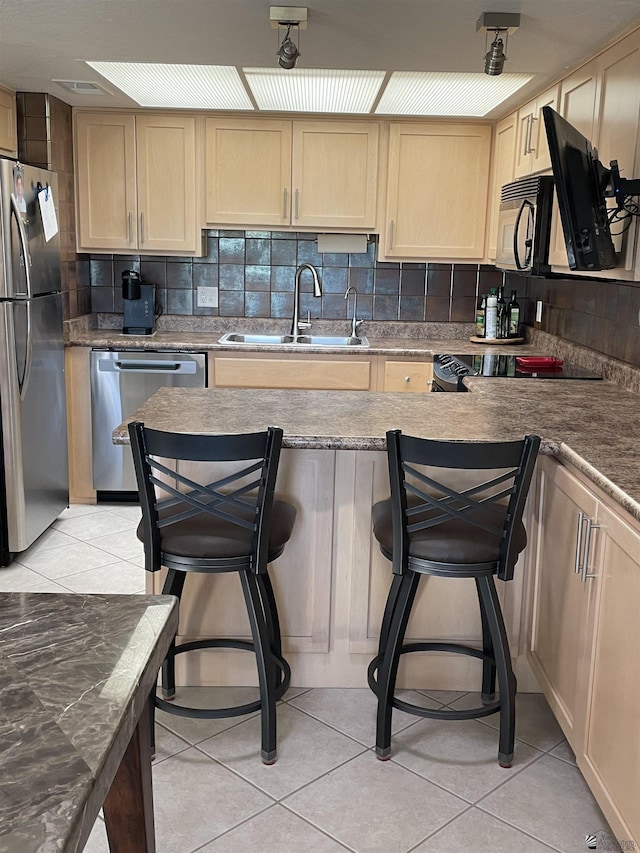 kitchen with sink, stainless steel appliances, tasteful backsplash, a kitchen bar, and light tile patterned floors