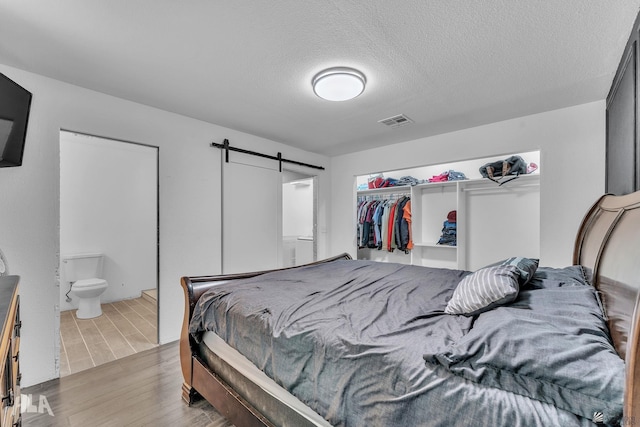 bedroom with ensuite bath, light hardwood / wood-style floors, a textured ceiling, a barn door, and a closet