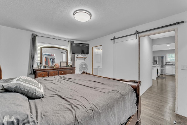 bedroom with stainless steel fridge with ice dispenser, wood-type flooring, a barn door, and a textured ceiling