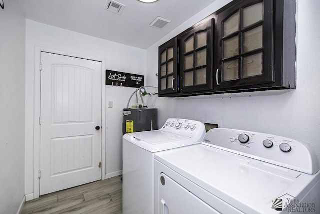 washroom featuring cabinet space, visible vents, independent washer and dryer, light wood-type flooring, and water heater