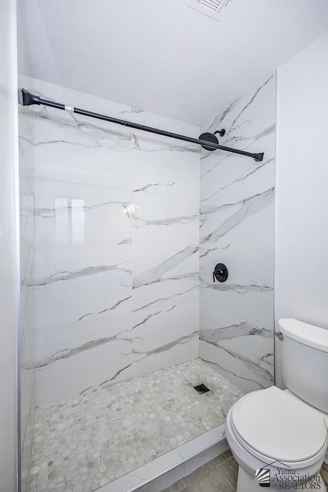 bathroom with wood finished floors, a marble finish shower, and toilet