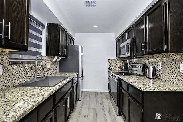 kitchen with light stone counters, stainless steel appliances, a sink, visible vents, and light wood finished floors