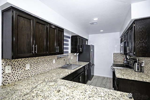 kitchen with light stone counters, a sink, visible vents, light wood finished floors, and tasteful backsplash