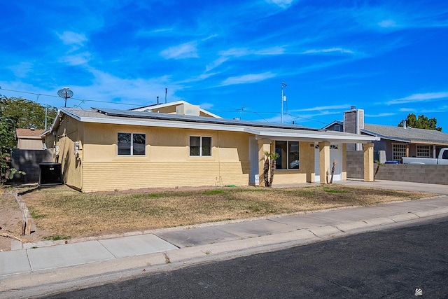 ranch-style house featuring a porch, a front yard, central air condition unit, and solar panels