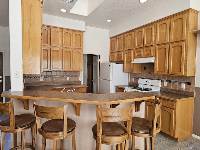 kitchen with a kitchen breakfast bar, kitchen peninsula, a textured ceiling, white appliances, and light tile patterned flooring