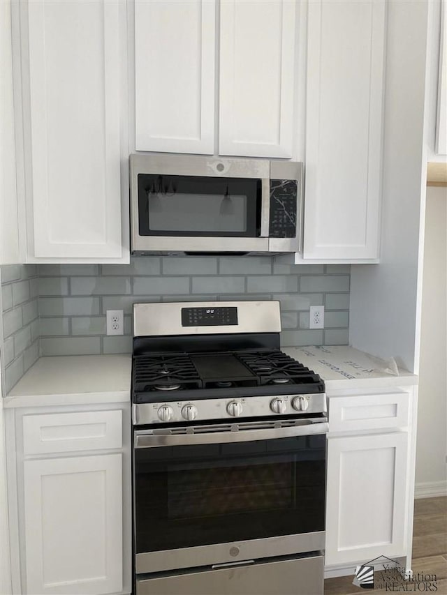 kitchen with backsplash, hardwood / wood-style floors, white cabinetry, stainless steel appliances, and light stone counters