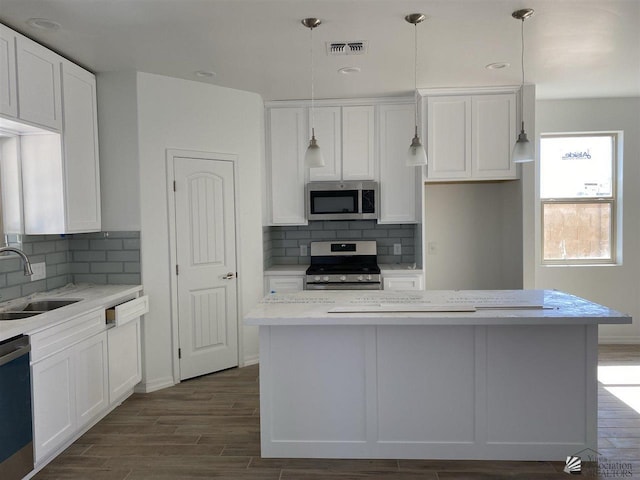 kitchen featuring decorative light fixtures, white cabinets, appliances with stainless steel finishes, and a kitchen island