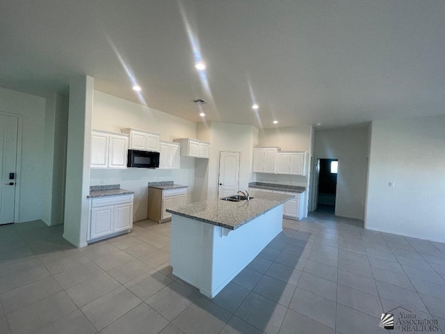 kitchen with white cabinets, light stone counters, a kitchen island with sink, and sink