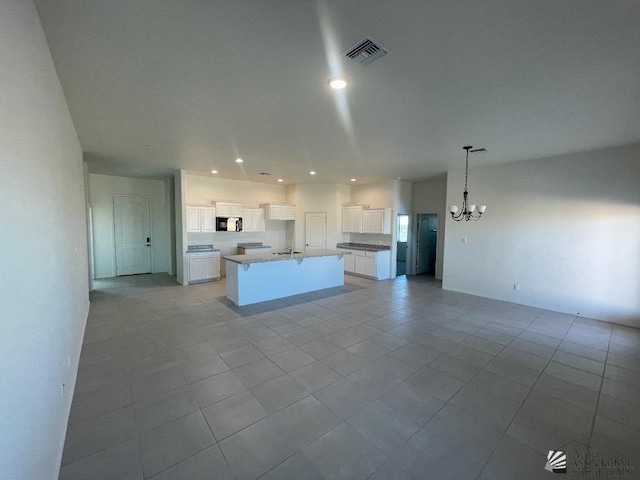 kitchen with a kitchen island with sink, sink, pendant lighting, an inviting chandelier, and white cabinets