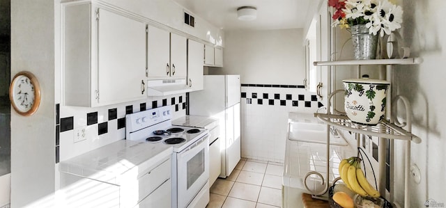 kitchen with white appliances, white cabinetry, tile walls, tile countertops, and light tile patterned floors