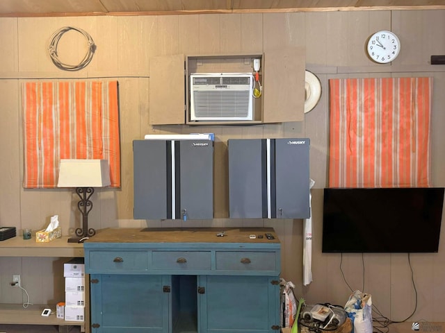 kitchen with an AC wall unit, blue cabinetry, and wooden walls