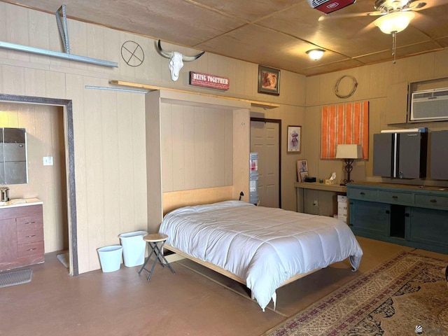 bedroom with ceiling fan, wood walls, concrete flooring, and sink