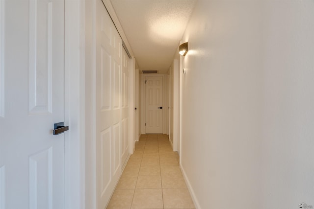 hall with light tile patterned floors, visible vents, baseboards, and a textured ceiling