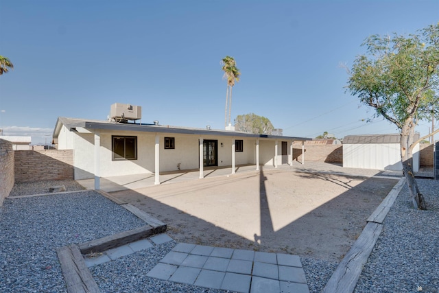 rear view of house with a fenced backyard, an outbuilding, central air condition unit, a patio area, and stucco siding