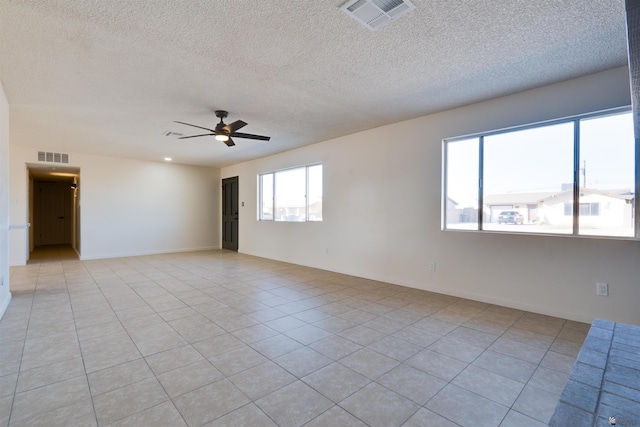 empty room featuring light tile patterned floors, a textured ceiling, visible vents, and a ceiling fan