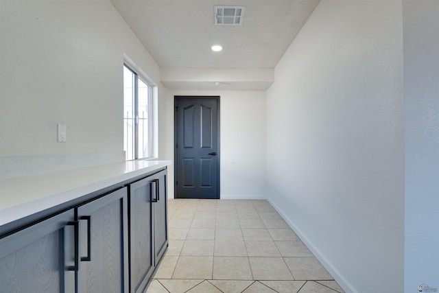 hall featuring light tile patterned floors, visible vents, and baseboards