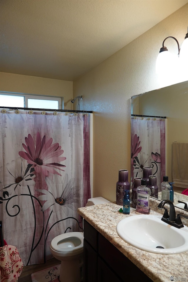 full bathroom featuring a textured wall, vanity, and toilet