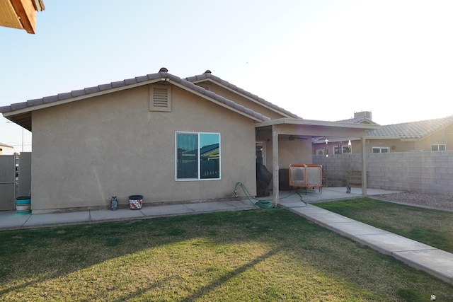 rear view of property featuring a patio, a tile roof, fence, a yard, and stucco siding