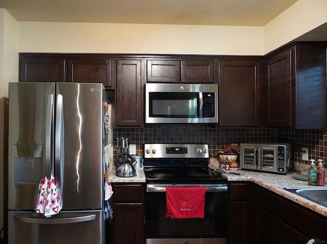 kitchen featuring dark brown cabinetry, a toaster, appliances with stainless steel finishes, backsplash, and a sink