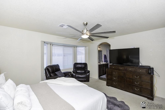 bedroom with ceiling fan, connected bathroom, light carpet, and a textured ceiling