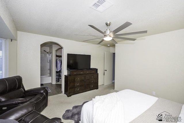 carpeted bedroom with ceiling fan, a walk in closet, a closet, and a textured ceiling