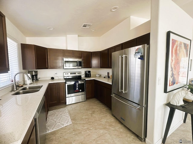 kitchen featuring visible vents, appliances with stainless steel finishes, a sink, dark brown cabinetry, and light stone countertops