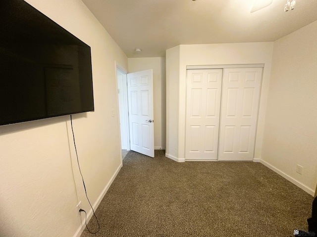 unfurnished bedroom featuring baseboards, dark carpet, and a closet