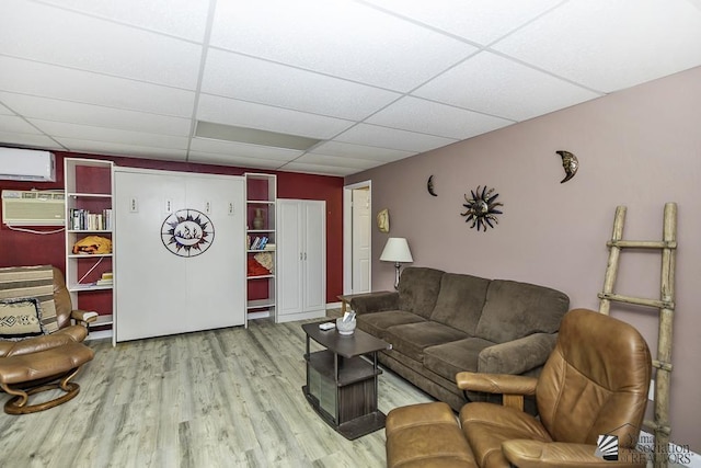 living room with hardwood / wood-style flooring, a wall mounted AC, and a drop ceiling