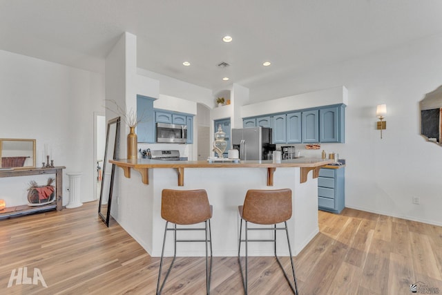 kitchen with blue cabinets, a breakfast bar area, light hardwood / wood-style flooring, appliances with stainless steel finishes, and kitchen peninsula