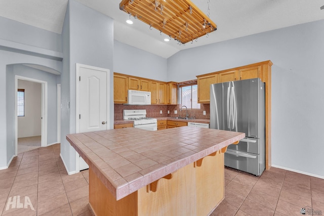 kitchen with white appliances, arched walkways, tile countertops, a center island, and a sink