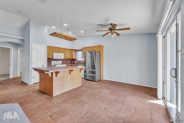 kitchen featuring arched walkways, light countertops, stove, freestanding refrigerator, and a kitchen island