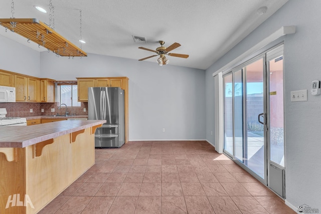 kitchen with range, white microwave, a kitchen breakfast bar, freestanding refrigerator, and light countertops